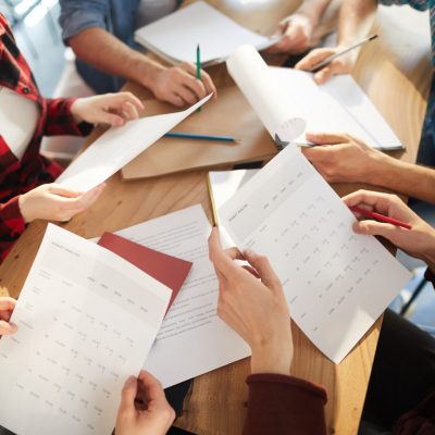View of business documents in hands of colleagues over workplace during working briefing